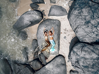 two beautiful mermaids are lying on the stones and sunbathing, top view