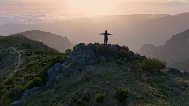 Man stands on top of mountain and looks at the sunrise sky. Aerial view of magnificent sunrise in the mountains of Madeira island. Climber in the mountains achieved his goal and enjoys wonderful