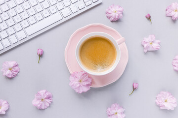 Computer keyboard and cup of espresso coffee on spring pink background with cherry blossom flowers. Home office, studying, distance learning, freelance, lifestyle, internet shopping concept. Top view