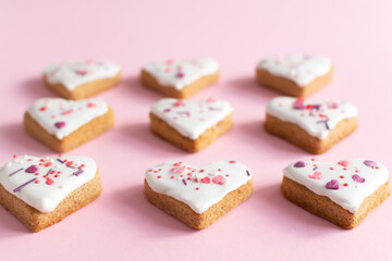 Gingerbread covered with white icing and sprinkling on a pink background. The concept of celebrating Valentine's Day. Horizontal orientation. Selective focus.