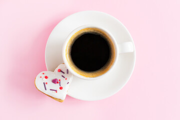 White cup and saucer with espresso and gingerbread covered with white icing and sprinkling on a pink background. The concept of celebrating Valentine's Day. Horizontal orientation. copy space.