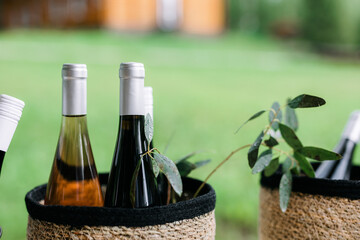 bar table. Closed wine bottles in wicker baskets on a table against a backdrop of greenery. Bottle of wine in a basket against a beautiful landscape. farmhouse style. Horizontal format with copy space