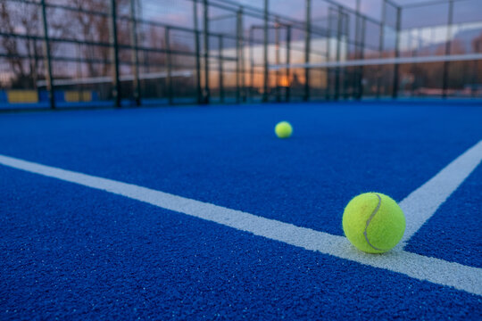 Selective focus. Paddle tennis ball in the foreground on the line of a blue paddle tennis court at sunset.