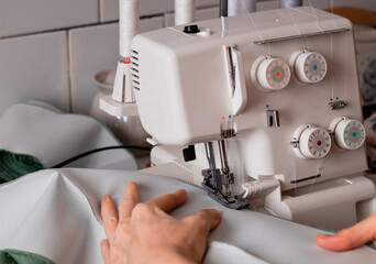Sewing machine overlock and womans hand of tailor. Sewing process on a white overlock.