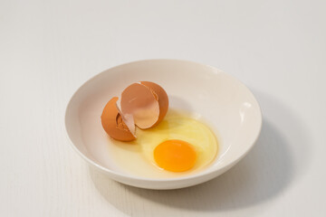 Raw chicken eggs beaten in a white plate. Yolk and around is white. The shell is on a plate.