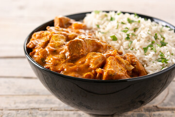Indian butter chicken in black bowl on wooden table. Close up