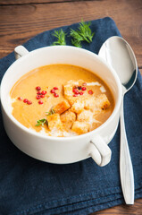 Delicious pumpkin soup  with cream and croutons in a white bowl on wooden table. Close up.