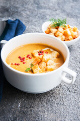 Delicious pumpkin soup with cream and croutons in a white bowl on grey background. Close up..