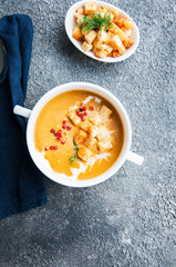 Delicious pumpkin soup with cream and croutons in a white bowl on grey background. Close up..