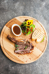 Grilled beef steak on a wooden board on a grey background. Top view.