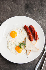 Fried eggs and sausages served on a white plate on a gray background.