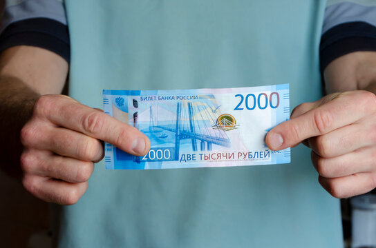 A Russian banknote with a face value of 2000 rubles in the hand of a man against the background of Russian money. The concept of finance, investment, savings and cash.