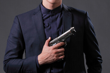 man in a suit holding a gun in hand on a gray background. soft focus.