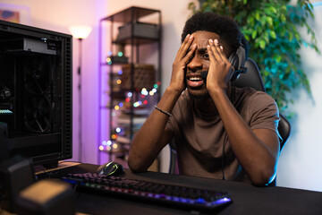 Professional pro video gamer playing on computer lost round in the game, he is heartbroken, disappointed, ashamed, the man covers face with hand, the room lit with led neon lights © ABCreative