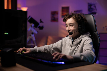 School-age child pro gamer spends time in front of the monitor playing computer games, laughing boy...
