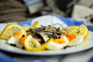 Herring fish fillets with eggs, herbs, onion and lemon on a white plate