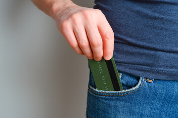 A young man takes out a credit card from his blue jeans pocket. Close-up on a man hand hand taking out a payment card from trousers on a light background.