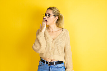 Young beautiful woman wearing casual sweater over isolated yellow background bored yawning tired covering mouth with hand. Restless and sleepiness.