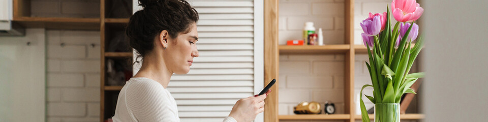 The side view of woman looking at phone while sitting at table in the kitchen