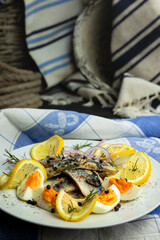 Herring fish fillets with eggs, herbs, onion and lemon on a white plate