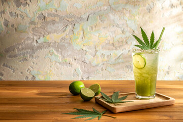 A glass of cannabis lemon soda with cannabis leaves in wooden tray on a wooden table over abstract...