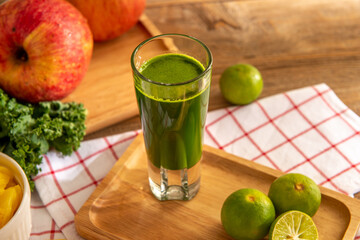 A glass of green flavor mixed fruit or vegetable juice serves in a tray with ingredients on wooden table over colorful abstract wall background. Eatable recipe health herb vegan juice drink concept