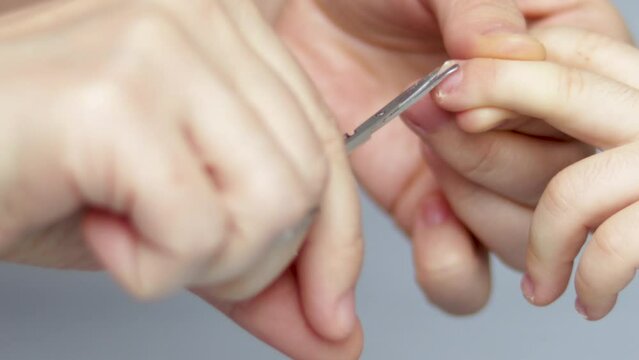 Close-up video of a mother, grandmother, woman or babysitter is cutting her little son's (or boy) nails with nail scissors, at home. care of the child. grey background.