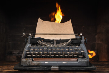 An old typewriter on the table on the burning flame in the fireplace background.