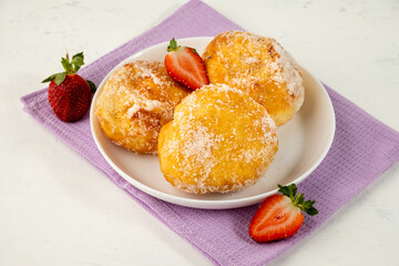 Malasada in a white plate three pieces with fresh strawberries. Portuguese donuts.