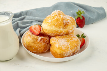 Delicious and fresh portuguese malasada donuts served with fresh strawberries on a white plate and milk.