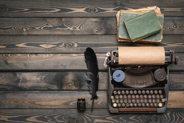 Retro style typewriter, quill pen and books on the wooden desk table background. Writer table.