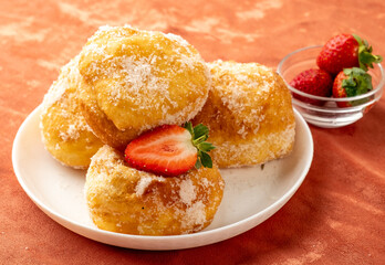 Portuguese donuts in a white plate with strawberries on a fabric background.
