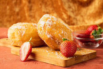 Malasada portuguese donuts on a wooden board with strawberries.