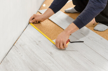 Fototapeta na wymiar Unrecognizable man laying laminate flooring. Professional laying of flooring - laminate. Measuring tape on laminate floor plank