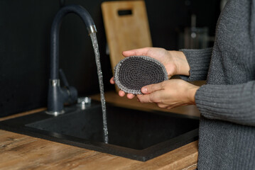 Hand holding natural reusable handmade knitted jute wash cloth at kitchen