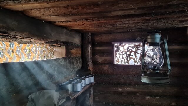 A wooden dugout in which a kerosene lamp burns. Light from the window penetrates into the room.