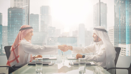 Two Successful Emirati Businessmen in White Traditional Kandura Sitting in Office and Signing Contract. Business Partners Shake Hands on Lucrative Investment. Saudi, Emirati, Arab Businessman Concept.