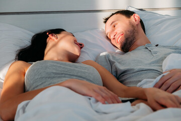 Young man and woman wake up in morning in bed and look at each other smiling. Beginning of a new day in happy family.