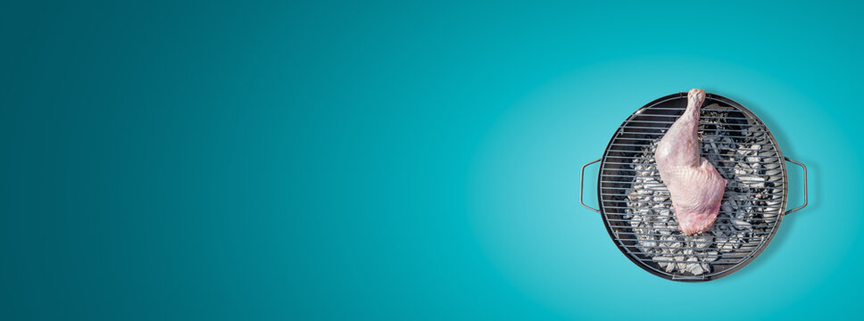 Banner with big chicken leg prepared for grill at a round barbeque firepan isolated at turquoise gradient background with copy space. Concept of food in outdoor cooking.