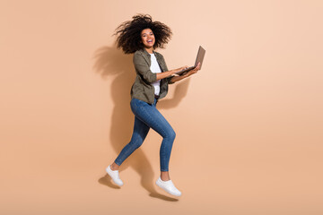 Fototapeta na wymiar Full length body size view of attractive cheerful girl jumping using laptop having fun isolated over beige pastel color background