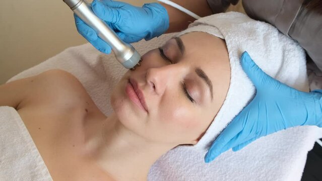 Young woman lying on cosmetologist's table during rejuvenation procedure. Cosmetologist take care about neck and face skin youthfull and wellness. Hardware face cleaning procedure  