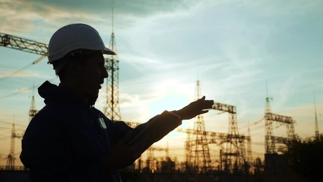 electrical power silhouette worker engineer a working with digital tablet, near tower with electricity. energy business technology industry concept. electrical studying reading documents on tablet