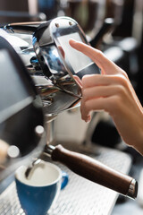Cropped view of barista using coffee machine near cup in cafe.