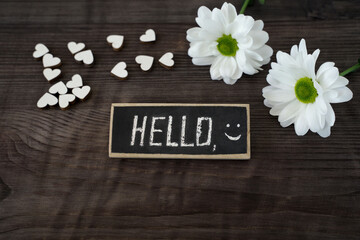 concept of the beginning of the day, spring and love. hello text and smile on blackboard. white daises and hearts on wooden background.