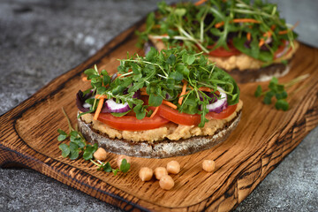 Sandwich toasted rustic bread with chickpea hummus, tomato slices, mix of lettuce and microgreens. Vegetarian breakfast. 