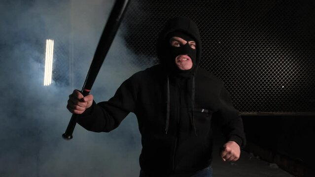 A man in a balaclava and with a baseball bat in his hands threatens