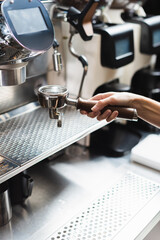 Cropped view of barista holding portafilter near coffee machine in cafe.