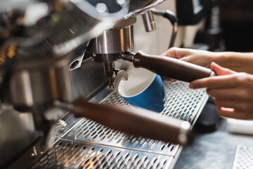 Cropped view of barista holding cup near coffee machine in cafe.