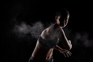 Fototapeta na wymiar Kickboxer kirl with magnesium powder on her hands, punching with dust visible.