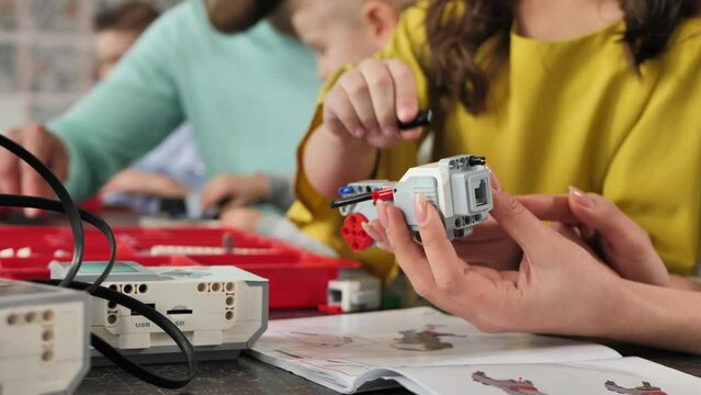 Close-up of a mother and daughter's hands at school making a robot controlled from a construction kit.